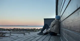 Kvinde set fra siden sidder alene ved havet